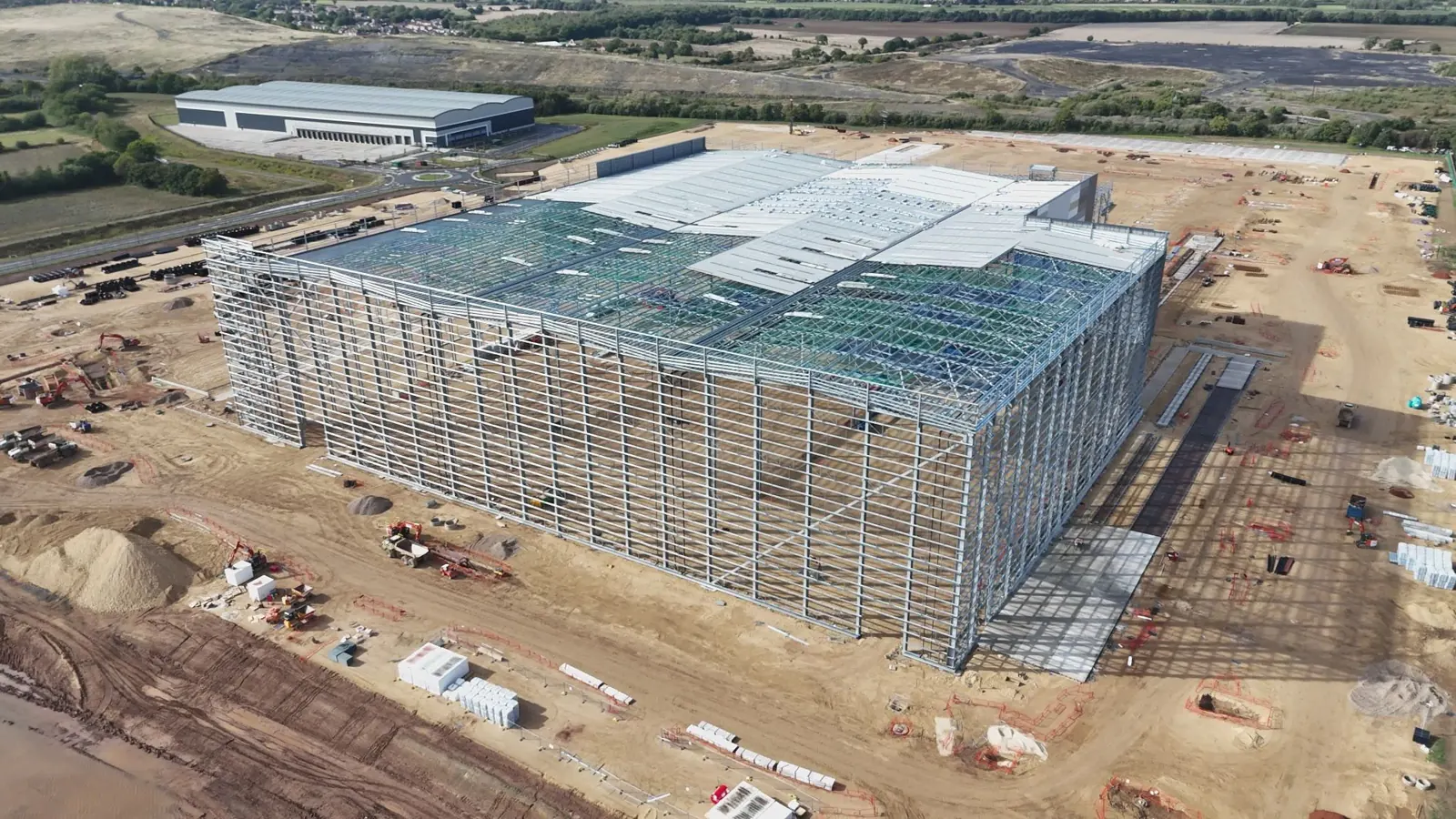 Aerial photograph of a large warehouse under construction with steel framing, equipment and nearby loading docks